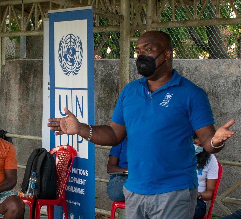 UN Volunteer with a face mask speaks to a group of people