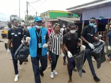 Refugee UN Volunteer Mbabazi Mugemana (in blue) participates in a clean-up campaign across Yaoundé's districts in June 2021. He is joined by footballer Ajara Nchout Njoya, youth from the DAFI programme, representatives from the refugee committees in Cameroonian communes and partners from Plan International.