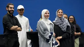 A group of smiling young women and men, standing and looking in one direction (right) and outside of the photo frame.