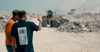 رجلان يراقبان الآلات الثقيلة لإزالة الأنقاض في منطقة مدمرة.