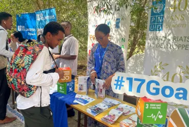 Young men and women talking by an outdoor table stand exhibiting UN-branded print materials