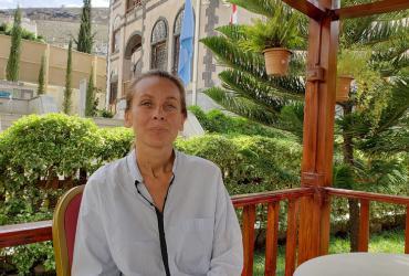 Maria Rosaria Bruno sitting in a garden. A building and the flags of the United Nations and the Republic of Yemen are showing in the background.