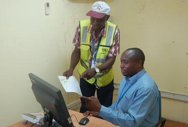 Patrick Ndalila (Kenya, standing), UN Volunteer Transport Dispatch Assistant with UNMIL, discusses work processes with a colleague in the mission.