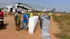 UN Volunteer Angeline Ambogo Kidiga, wearing a blue vest, stands beside stacks of electoral materials being unloaded from a UN helicopter, coordinating logistics and operations in Kaga Bandoro.